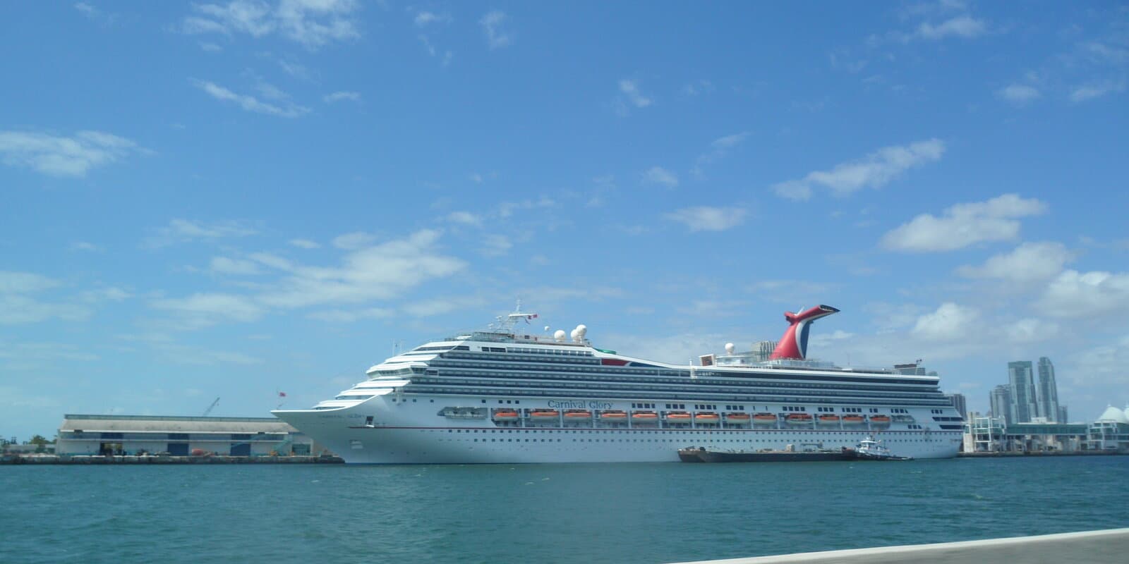 Carnival Glory cruise ship docked at PortMiami with the Miami skyline and cruise terminal visible across turquoise harbor water