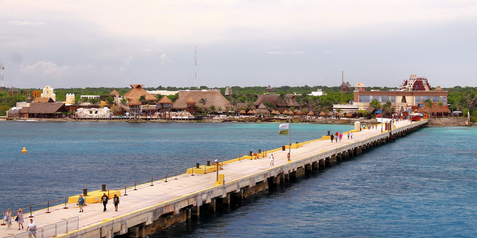 Long cruise pier with yellow safety rails leading to Costa Maya port buildings and thatched-roof structures in Quintana Roo, Mexico