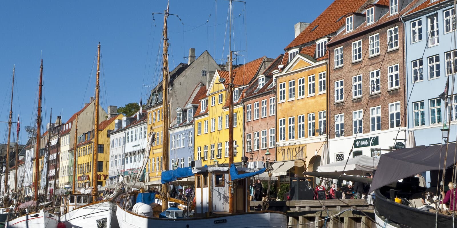 Colorful historic townhouses lining Nyhavn canal in Copenhagen with wooden sailing ships moored along the quay under a clear blue sky