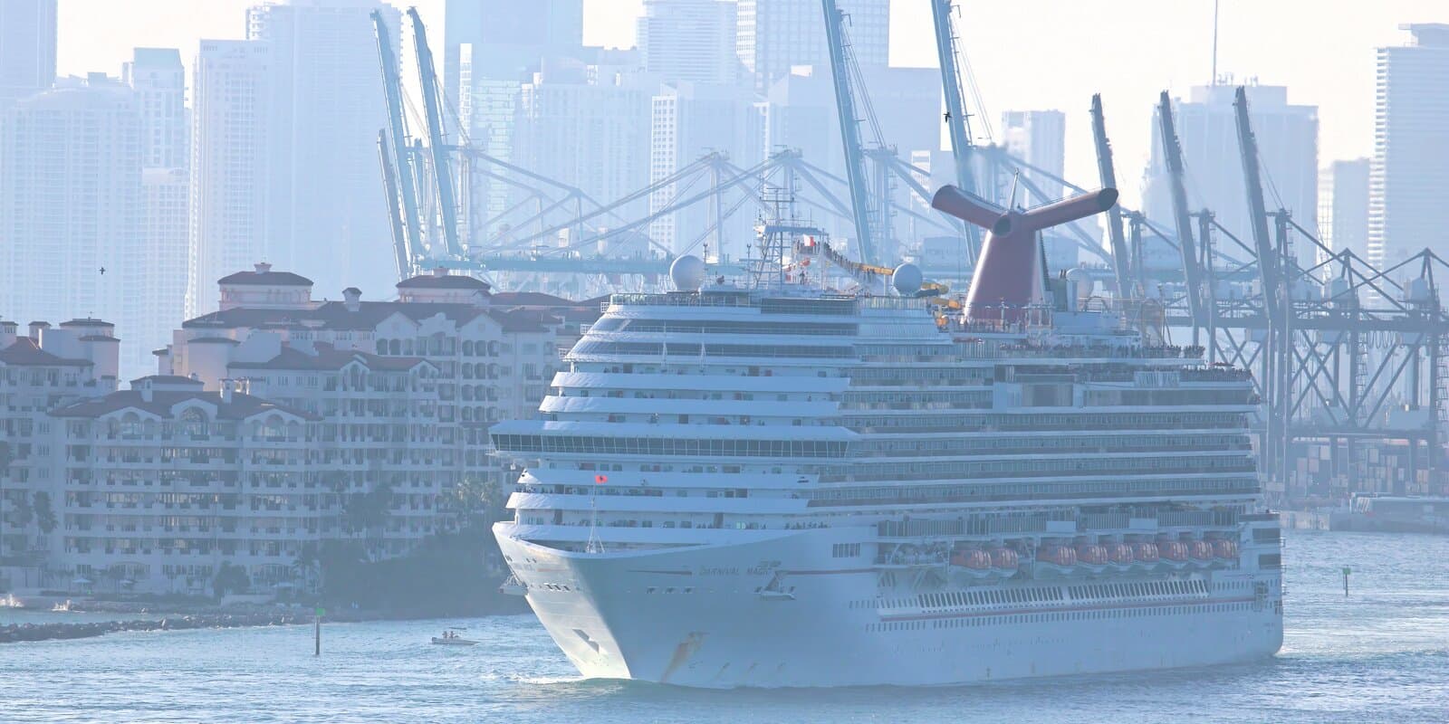 Carnival Magic cruise ship with red, white, and blue funnel departing Miami with the downtown skyline in the background