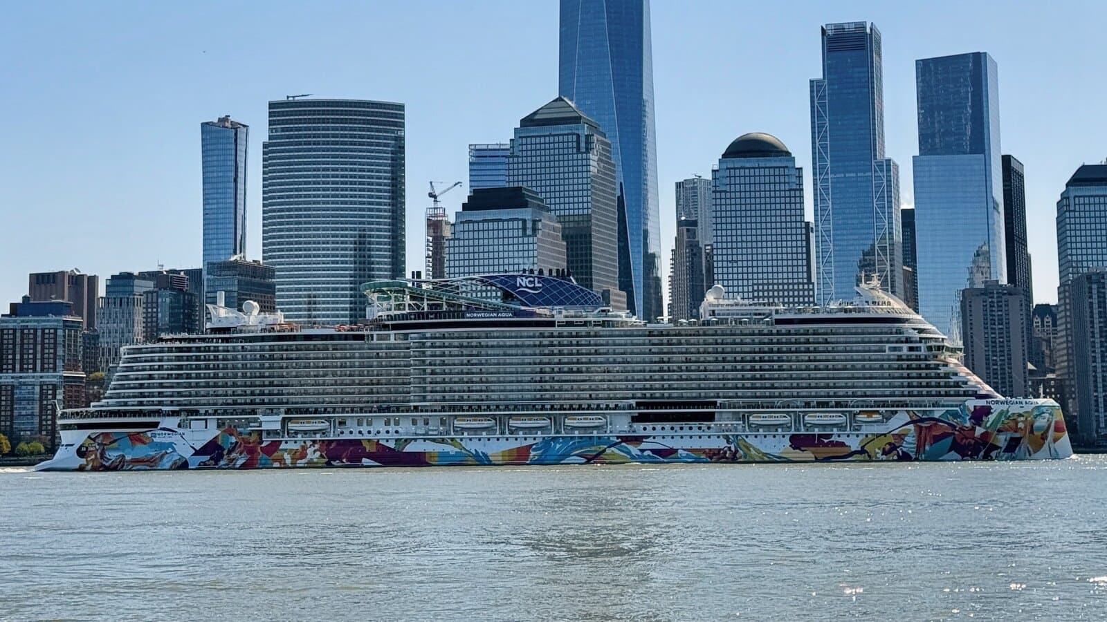 Norwegian Aqua cruise ship with colorful hull art passing the Lower Manhattan skyline on the Hudson River