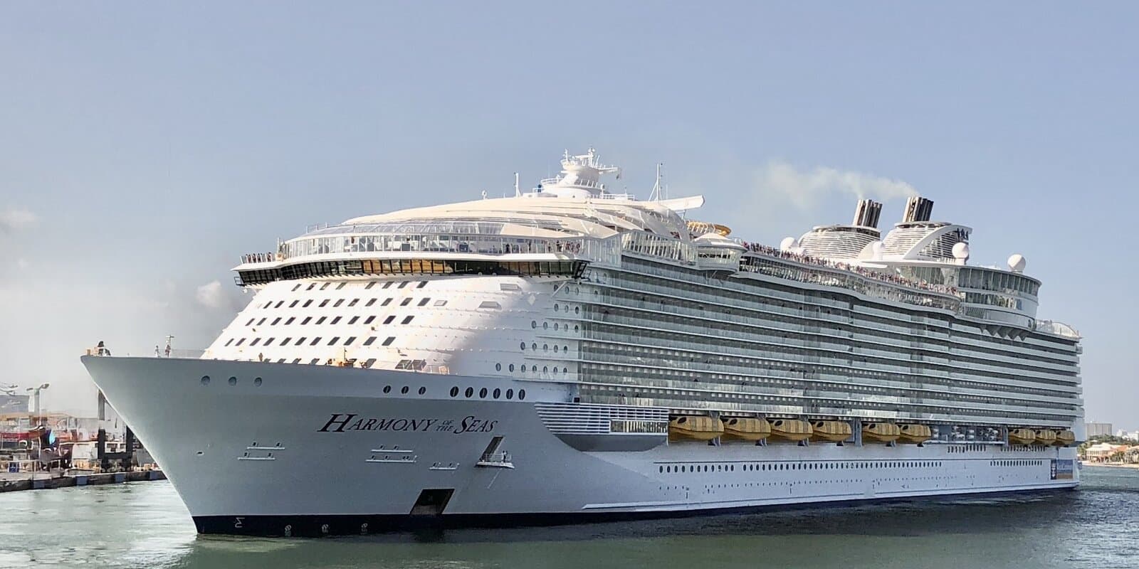 Harmony of the Seas, a Royal Caribbean International cruise ship, seen in profile on calm green water with the ship name visible on the bow